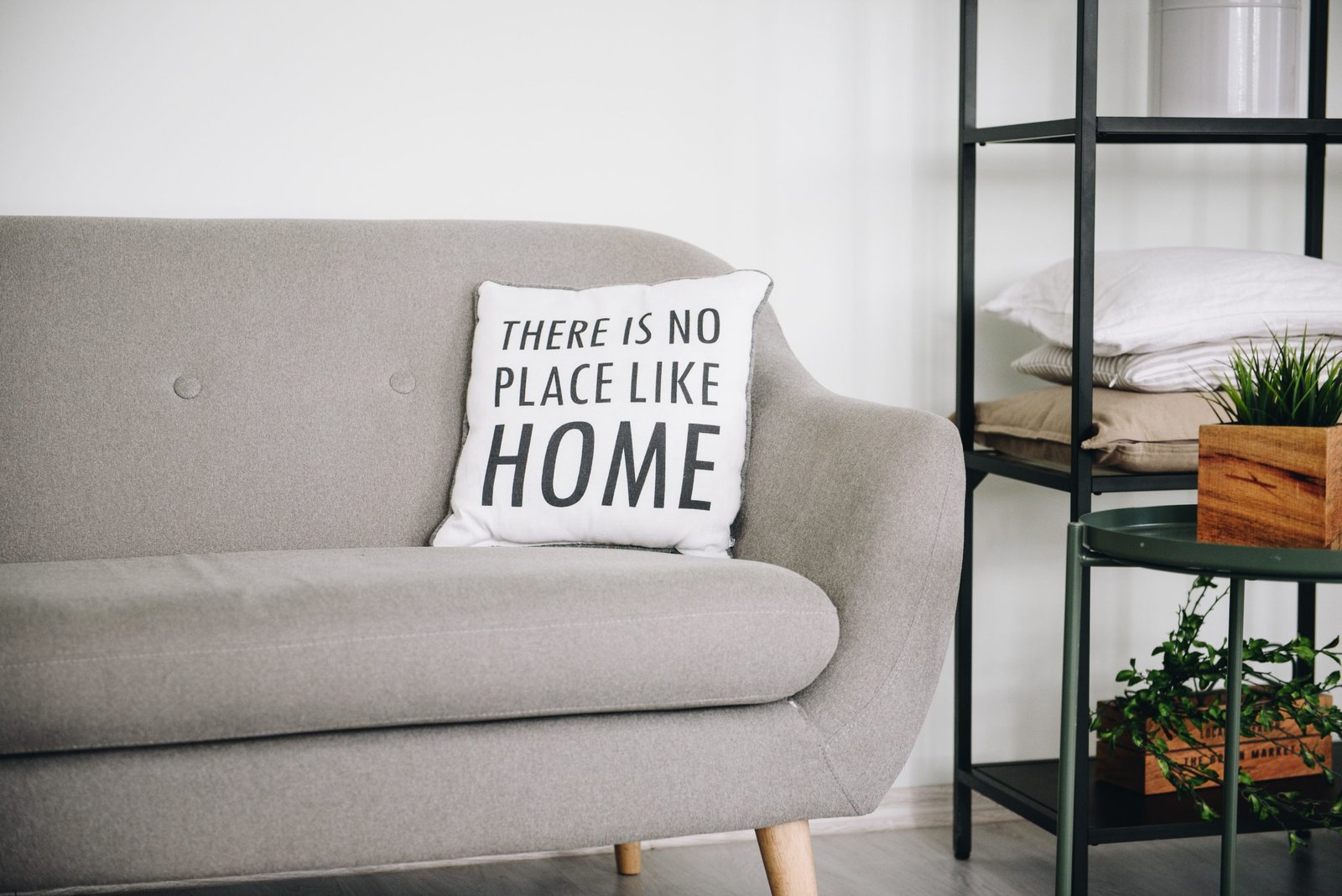 Gray sofa with a decorative pillow reading 'There is no place like home,' next to a shelf, set up through a professional furniture assembly service.